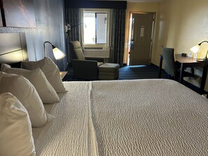 Une chambre d’hôtel avec un grand lit, un bureau, une chaise et une fenêtre avec des rideaux.