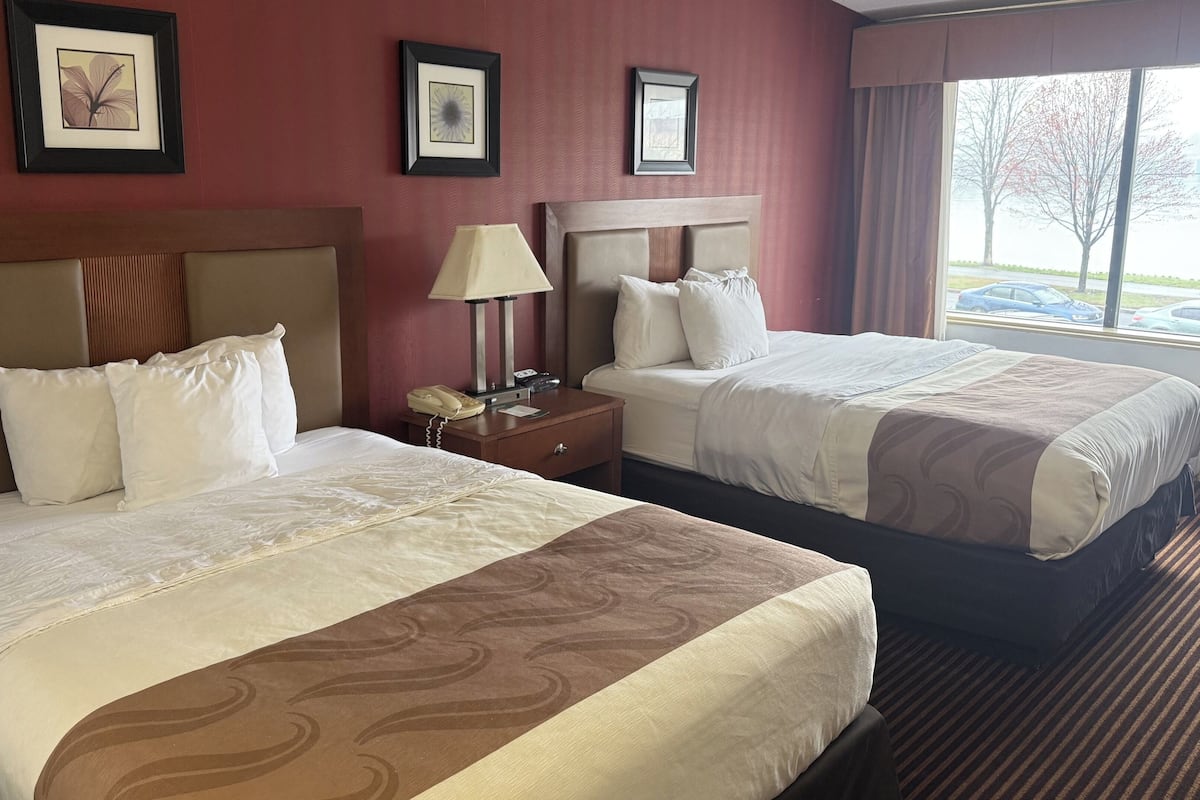 Een hotelkamer met twee bedden, een nachtkastje met een lamp en lijstwerken aan de muur.