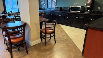 Una cocina moderna con armarios oscuros, un microondas, una cafetera y una zona de comedor con sillas y mesas de madera.