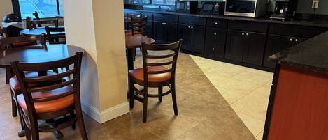 A modern kitchen with dark cabinets, a microwave, a coffee maker, and a dining area with wooden chairs and tables.