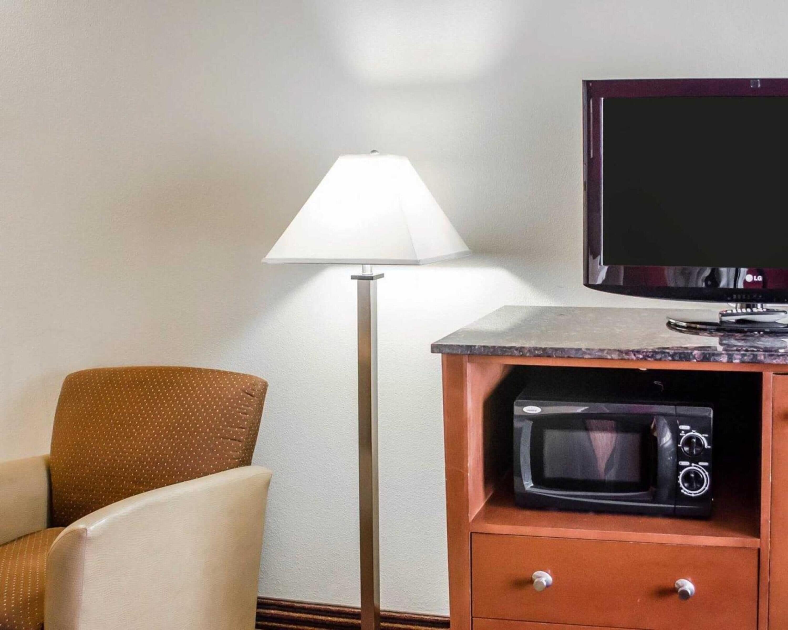 A hotel room with a sofa, a floor lamp, a flat-screen TV, and a microwave.