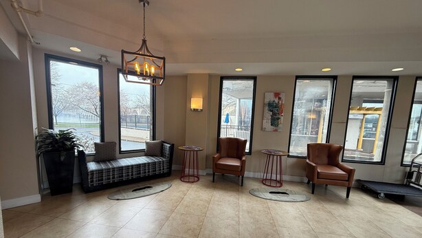 A spacious lobby with a large window, a bench, two chairs, a small table, and a hanging light fixture. - Hotel Hanna (Harrisburg)