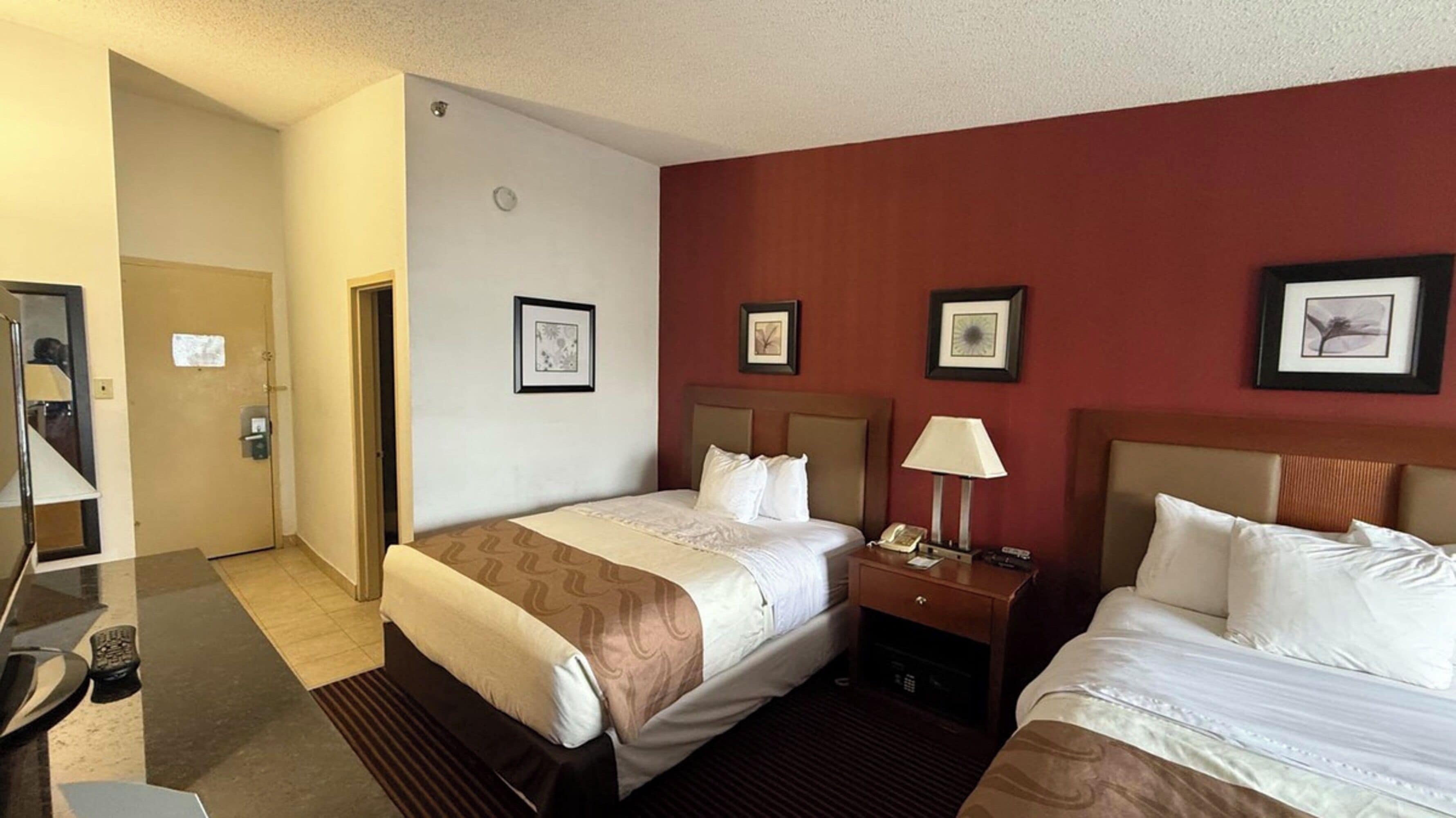 Ein Hotelzimmer mit zwei Betten, einem Schreibtisch mit Lampe, einem Telefon und gerahmten Bildern an der Wand.