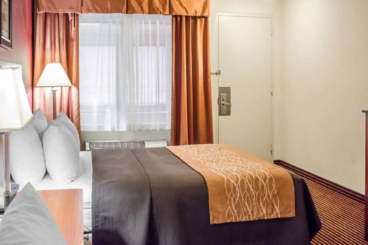 Een hotelkamer met een bed, nachtkastje, lamp en raam met gordijnen.