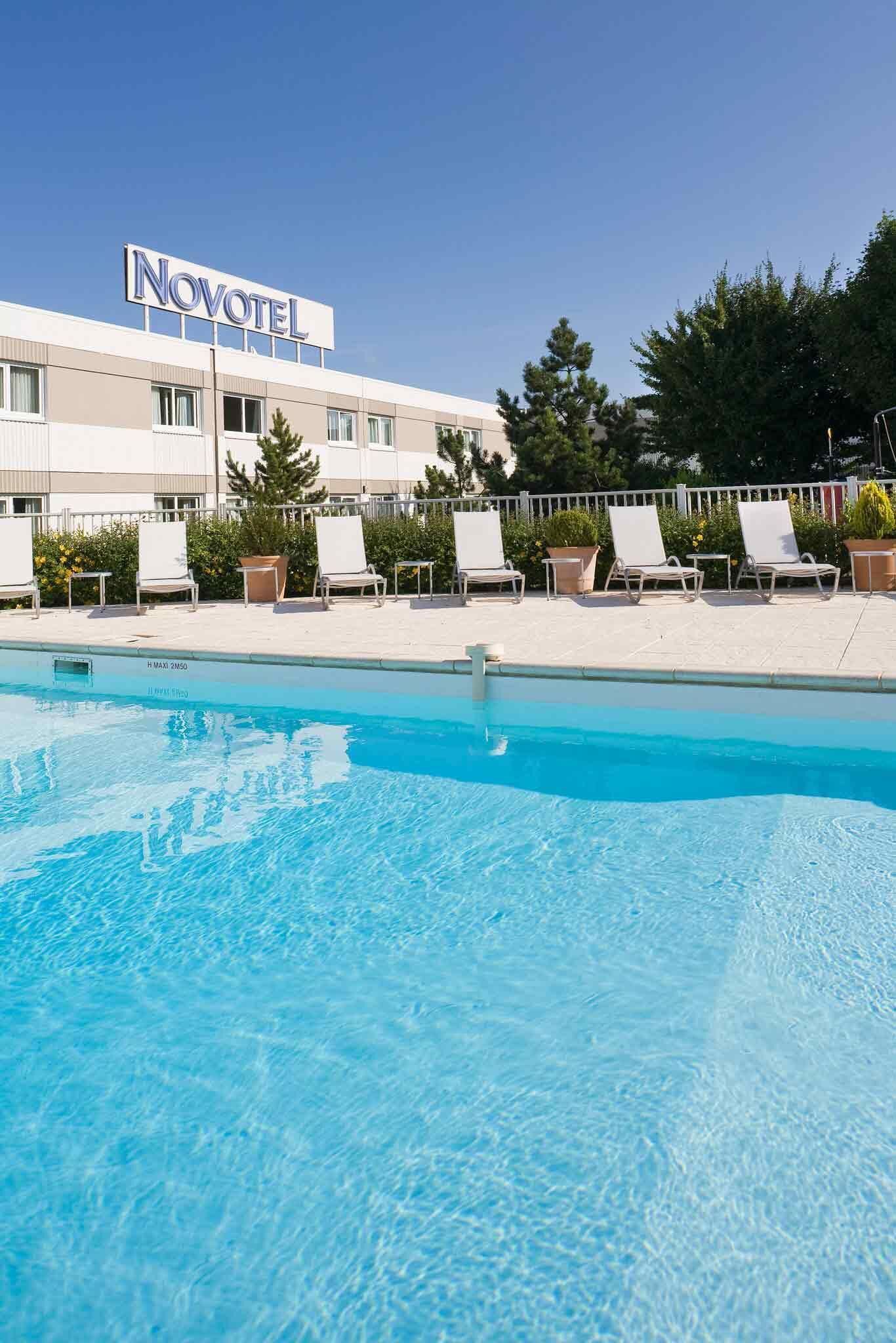 A Novotel hotel with a swimming pool, lounge chairs, and a clear blue sky.