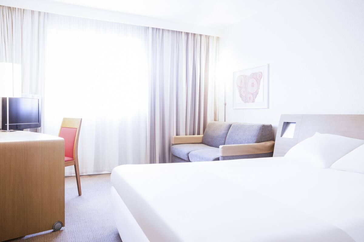 Une chambre d’hôtel équipée d’un lit, d’un bureau, d’une chaise, d’une télévision et d’une fenêtre avec des rideaux.