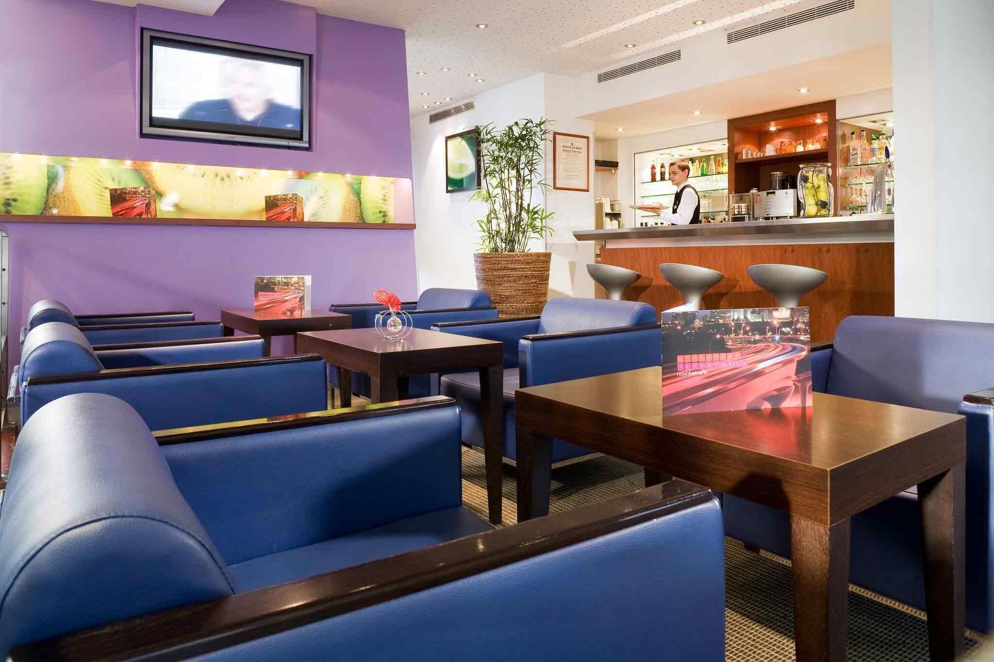 Un hall de hotel con asientos azules, una zona de bar y un televisor montado en la pared.