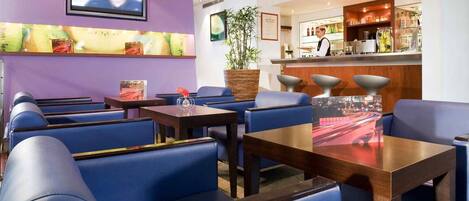 A hotel lobby with blue seating, a bar area, and a television mounted on the wall.