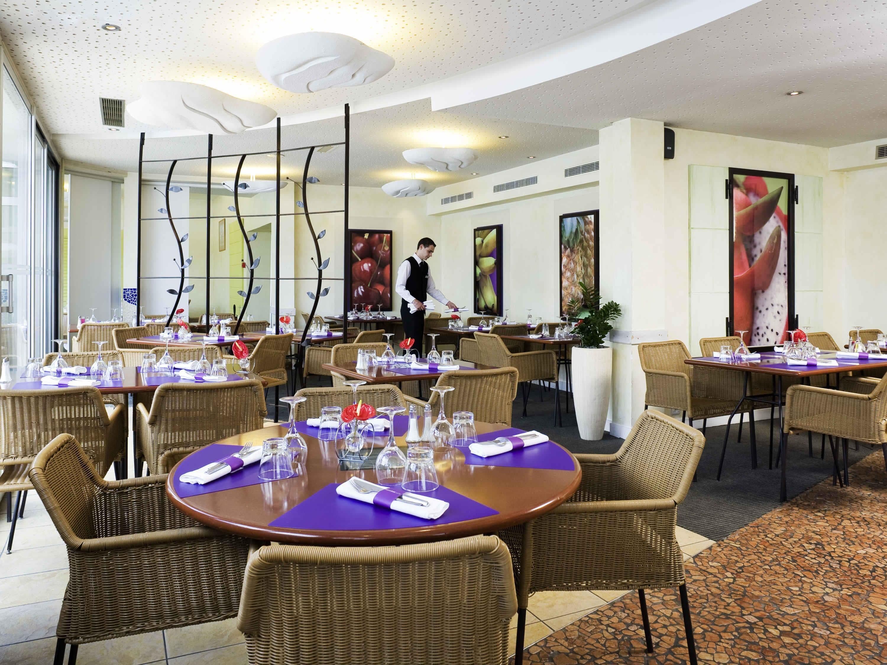 Een restaurant met ronde tafels, rieten stoelen en een ober.
