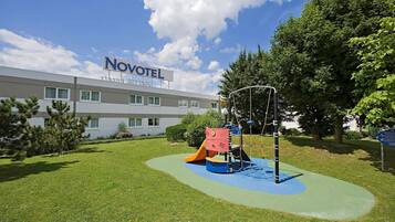 Explore the hotel's playground area with a slide and climbing structures, set amidst lush greenery and a modern building design.