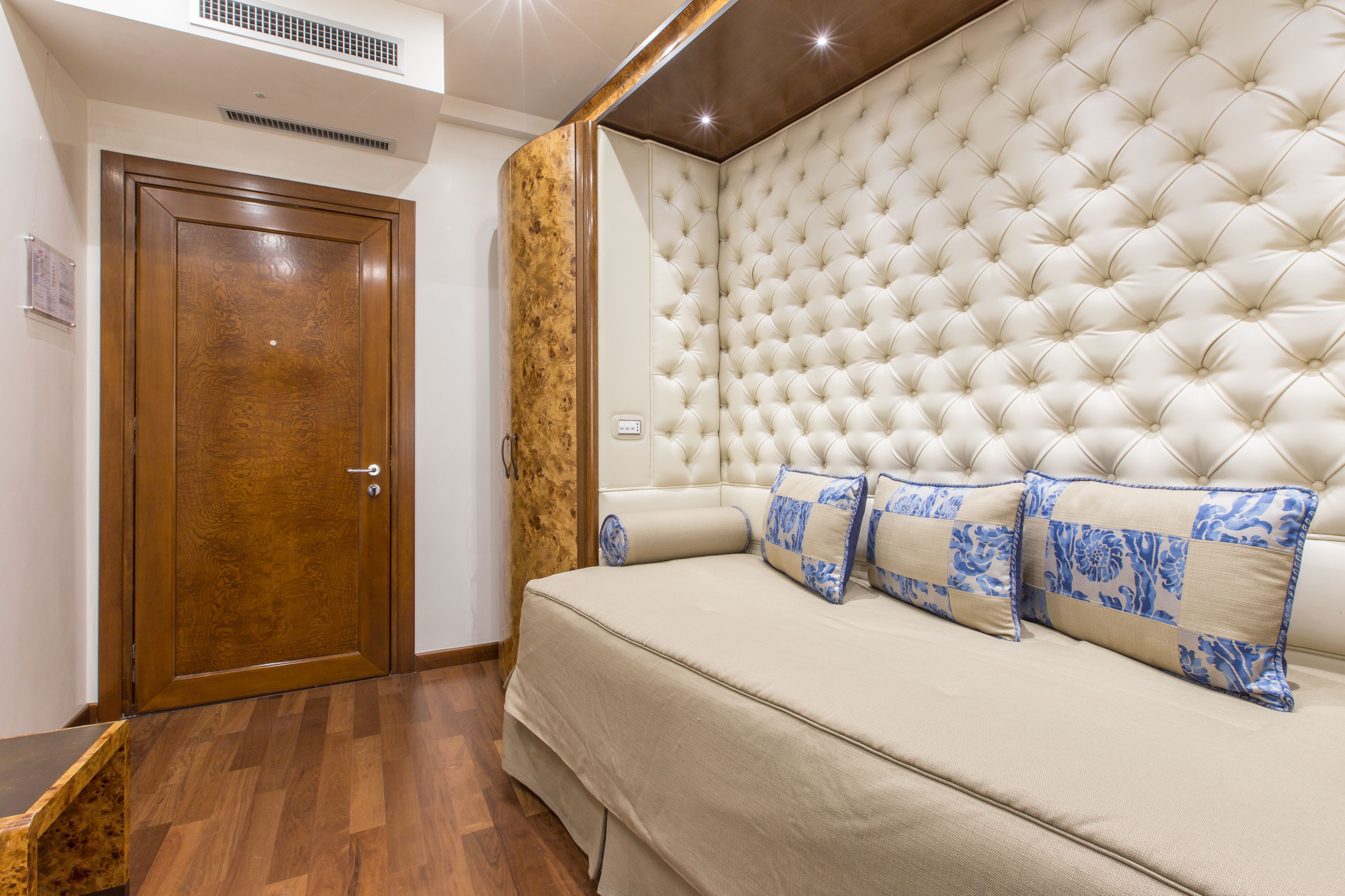 A bedroom with a wooden door, a tufted headboard, and a beige sofa with blue patterned pillows.