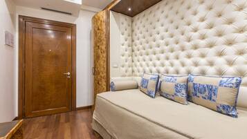 A bedroom with a wooden door, a tufted headboard, and a beige sofa with blue patterned pillows.