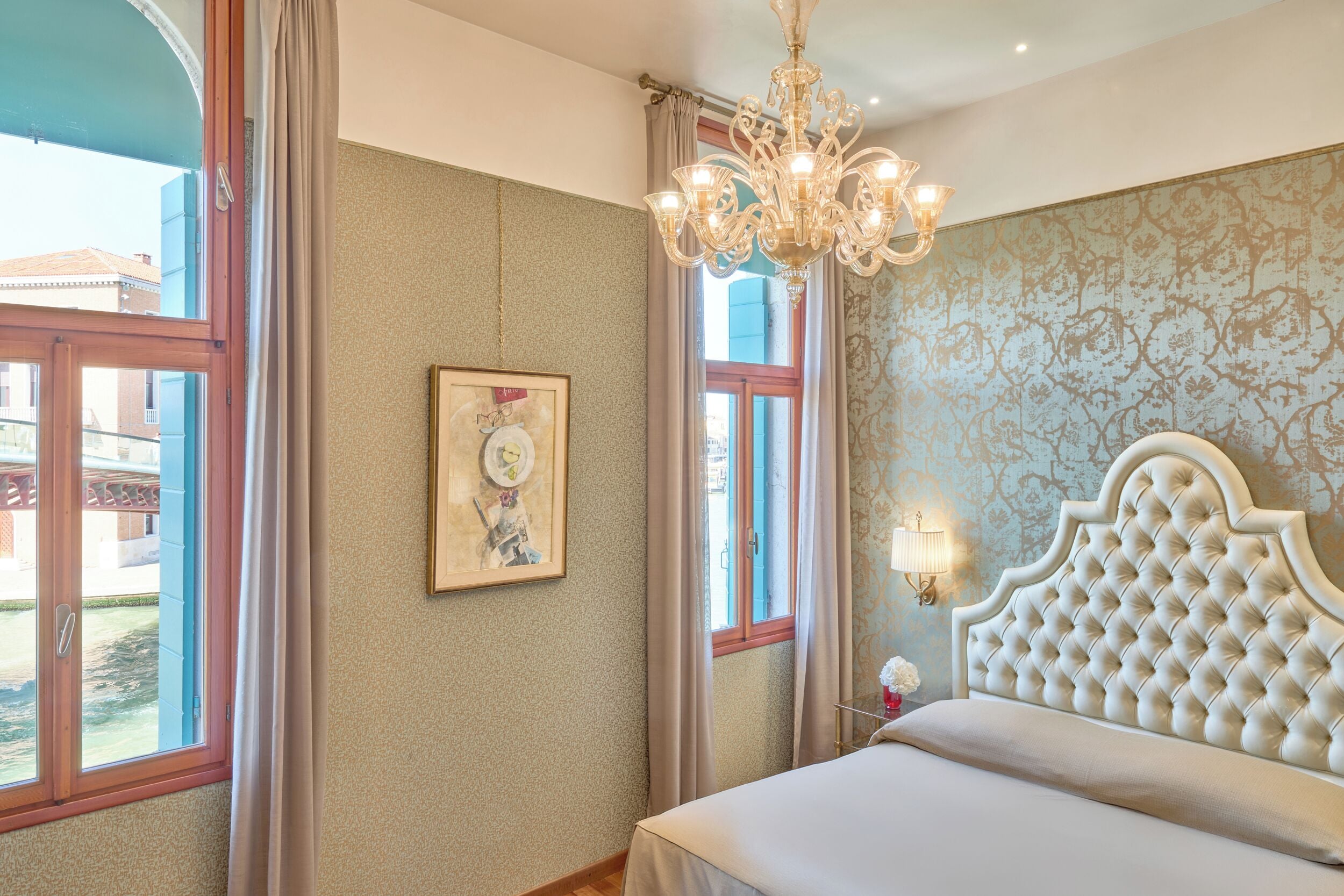 A bedroom with a large bed, a chandelier, a window with curtains, and a wall-mounted light fixture.
