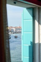 Vista da una stanza con finestra su un canale, con edifici e imbarcazioni.