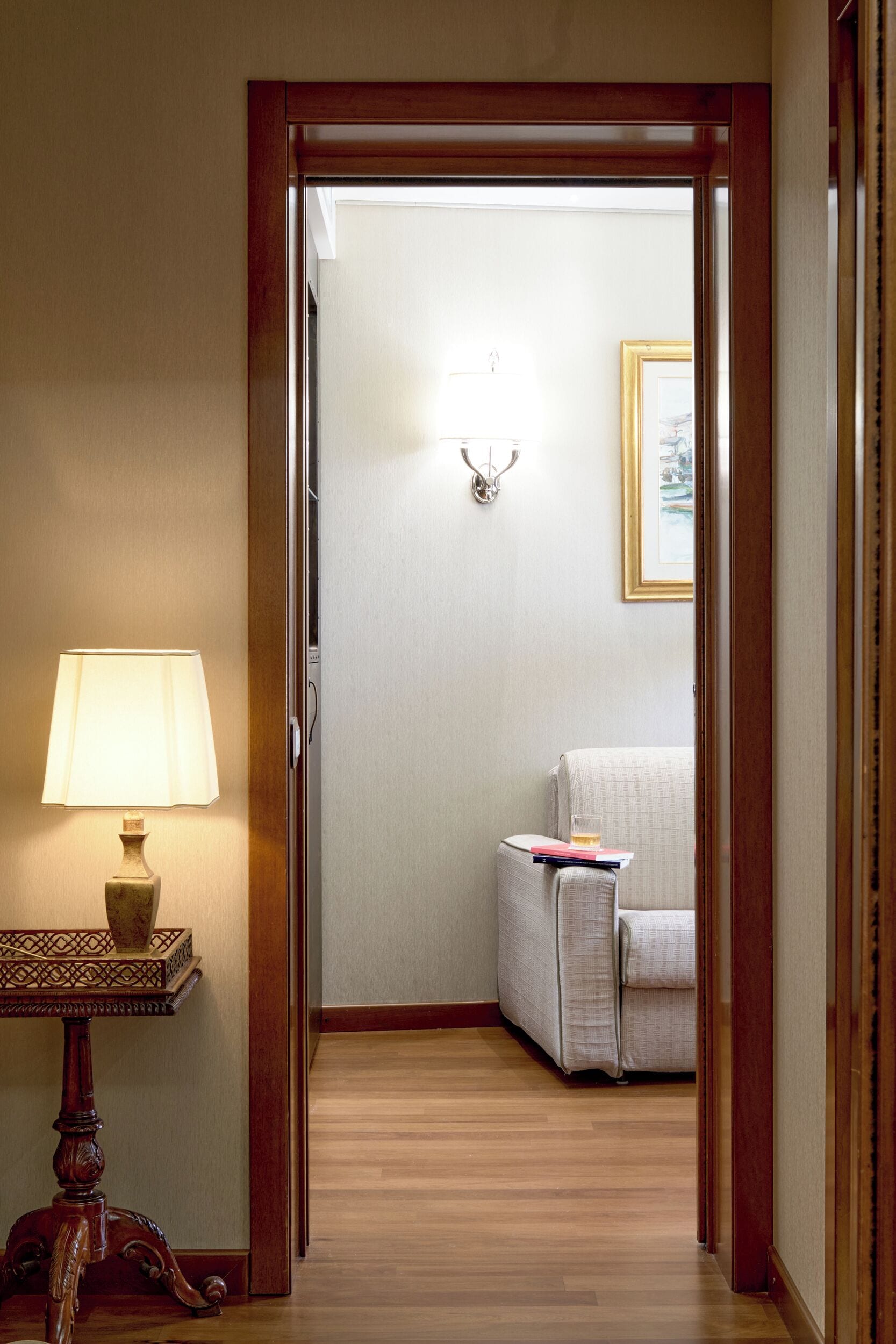 Un pasillo de hotel con una puerta de madera, una lámpara, una mesita y una silla.