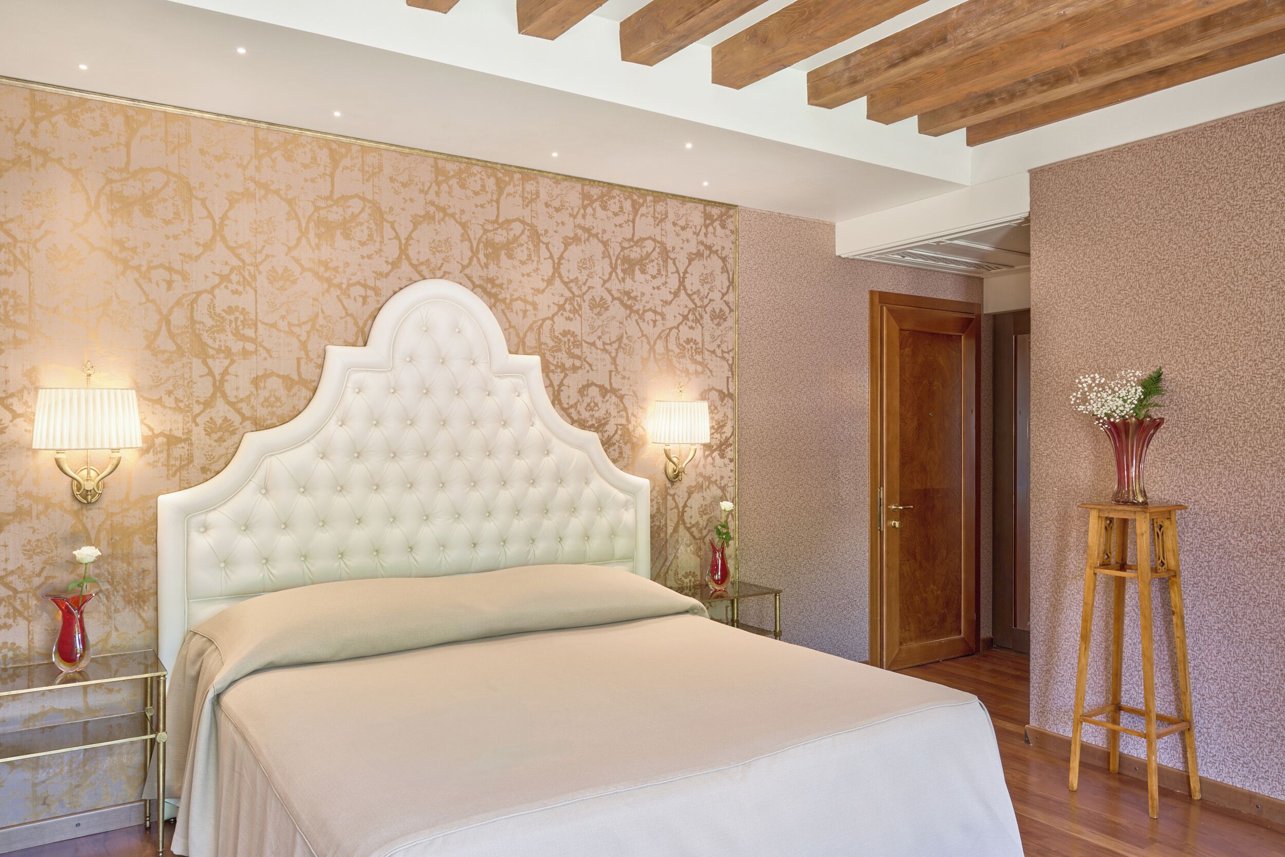 Camera da letto con una testiera trapuntata, due abat-jour, pavimento in legno e una porta sullo sfondo.