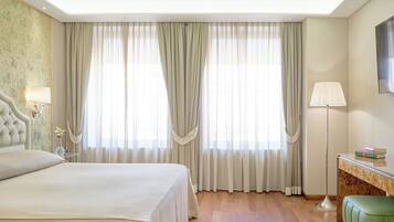 A hotel room with a large bed, a desk with a lamp, and a view of the outdoors through sheer curtains.