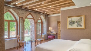 A bedroom with a large bed, wooden beams, stone arches, and a painting on the wall. - Santa Chiara Hotel (Venice)