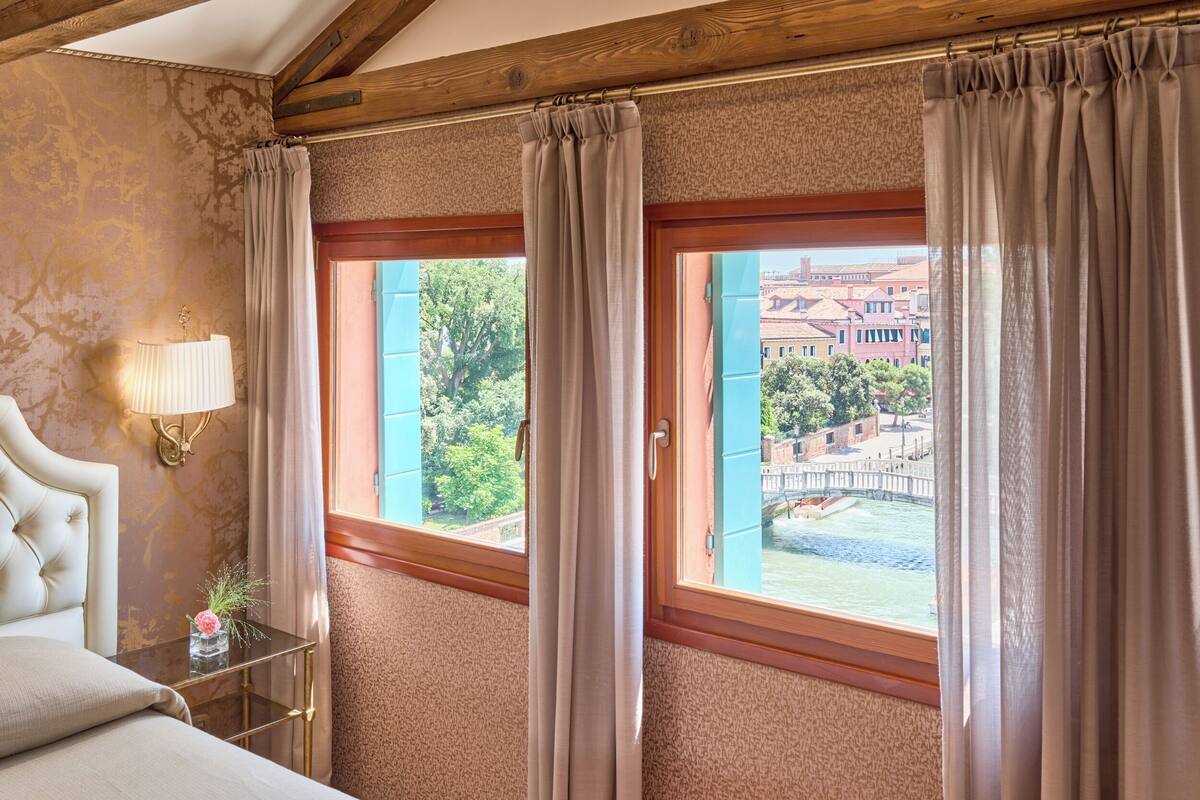A hotel room with a bed, a bedside table with a lamp, and a window with curtains.