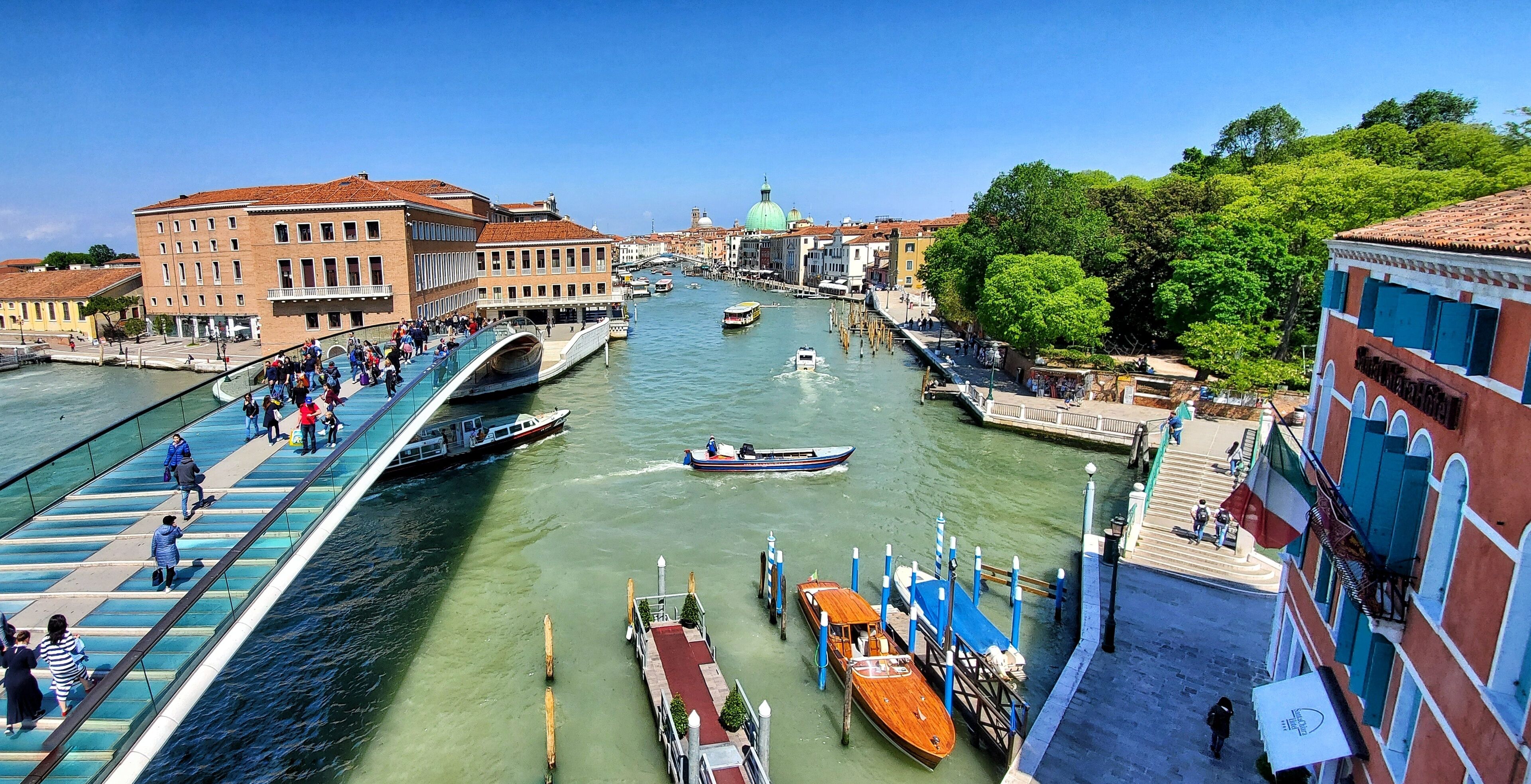 A canal with boats, a pedestrian bridge, and historic buildings along the water.