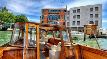 Una barca di legno con una cabina, un’area pranzo e vista sull'Hotel Santa Chiara e altri edifici sullo sfondo.