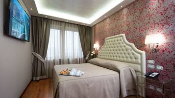 Une chambre d’hôtel dotée d’un grand lit, d’un téléviseur à écran plat fixé au mur, d’une table de chevet avec une lampe et d’un papier peint à motifs floraux.