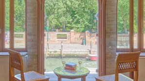 A room with two wooden chairs and a small table, a stone wall, and a view of a garden. - Santa Chiara Hotel (Venice)