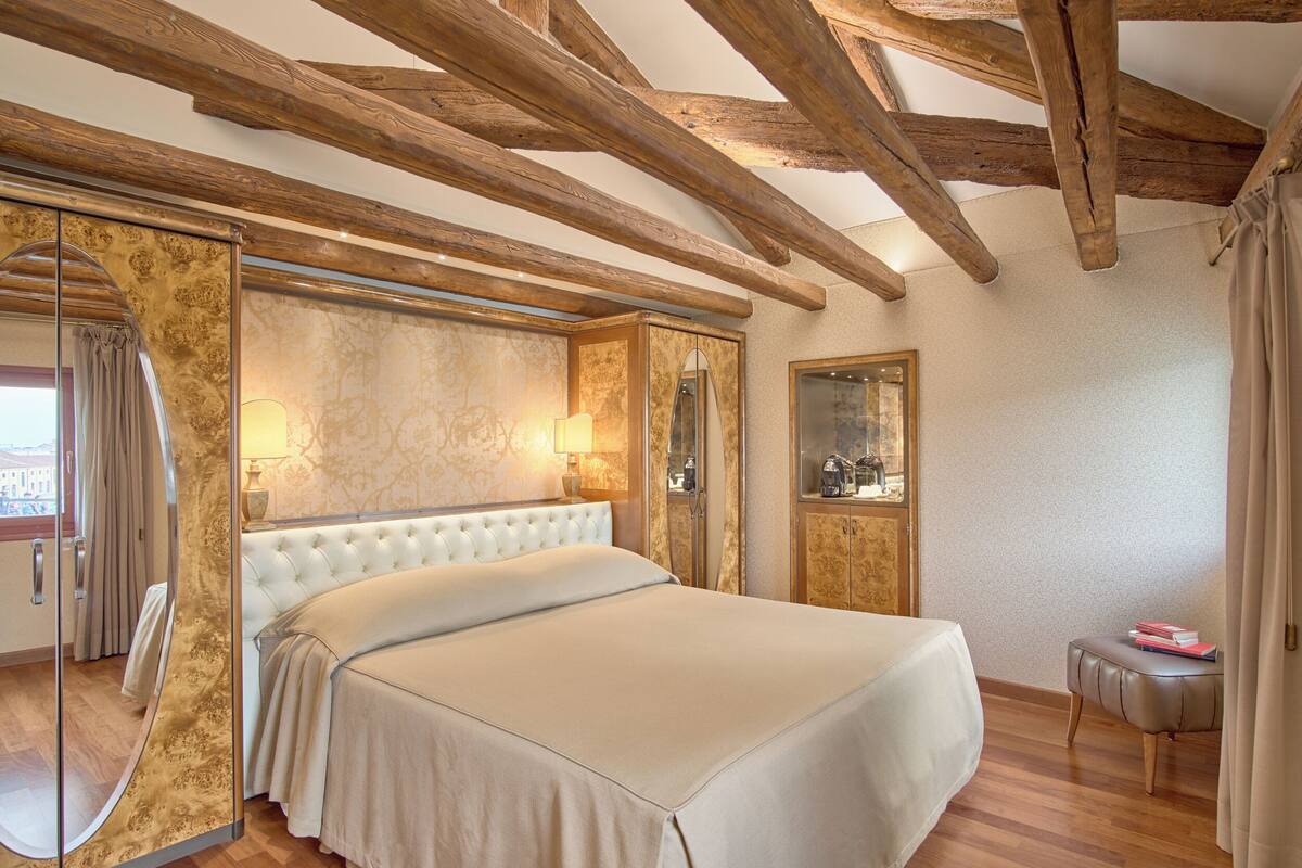 A bedroom with a large bed, wooden beams, a glass door, and a small table with books.