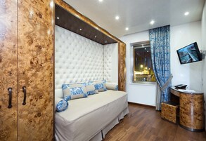 A bedroom with a large bed, a wardrobe, a television, and a window with curtains.