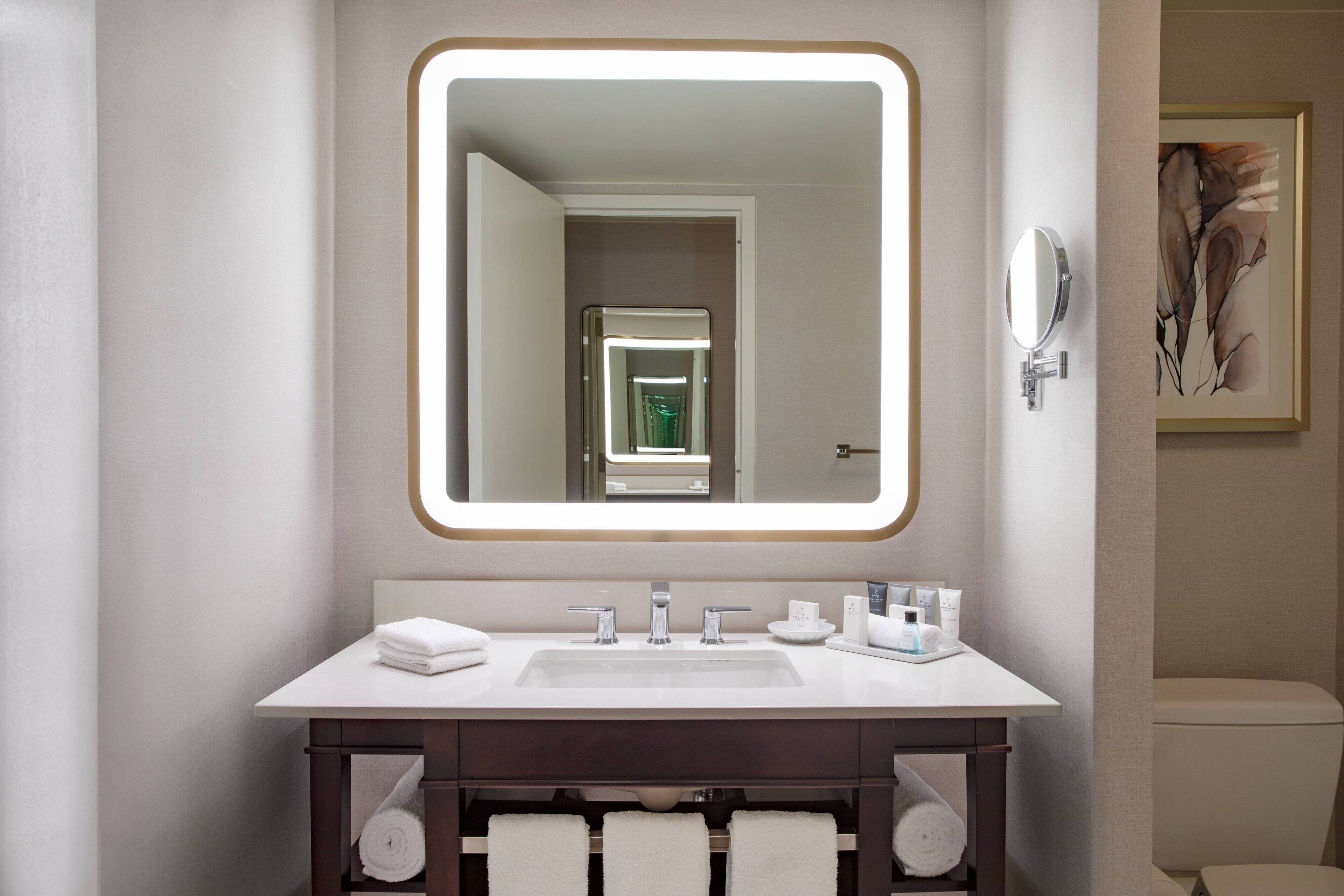 A modern bathroom with a large mirror, white sink, and dark vanity.