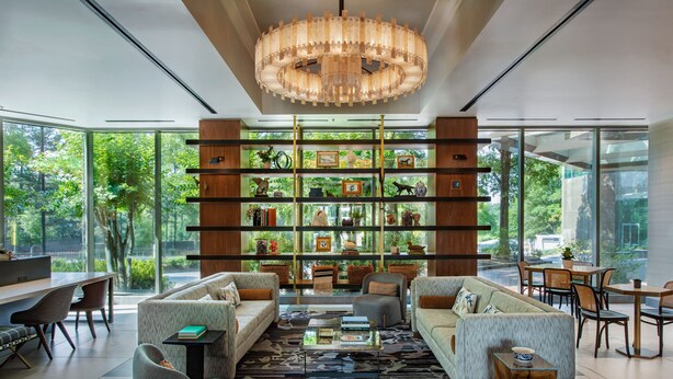 A modern living room with a large chandelier, a bookshelf filled with decorative items, and a view of greenery outside. - JW Marriott Atlanta Buckhead (Atlanta)