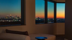 A modern living room with a sofa and a small table, large windows offering a city skyline view at dusk. - JW Marriott Atlanta Buckhead (Atlanta)