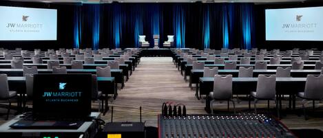 A conference room with rows of chairs, a stage with a screen displaying the JW Marriott Atlanta Buckhead logo, and audio equipment.