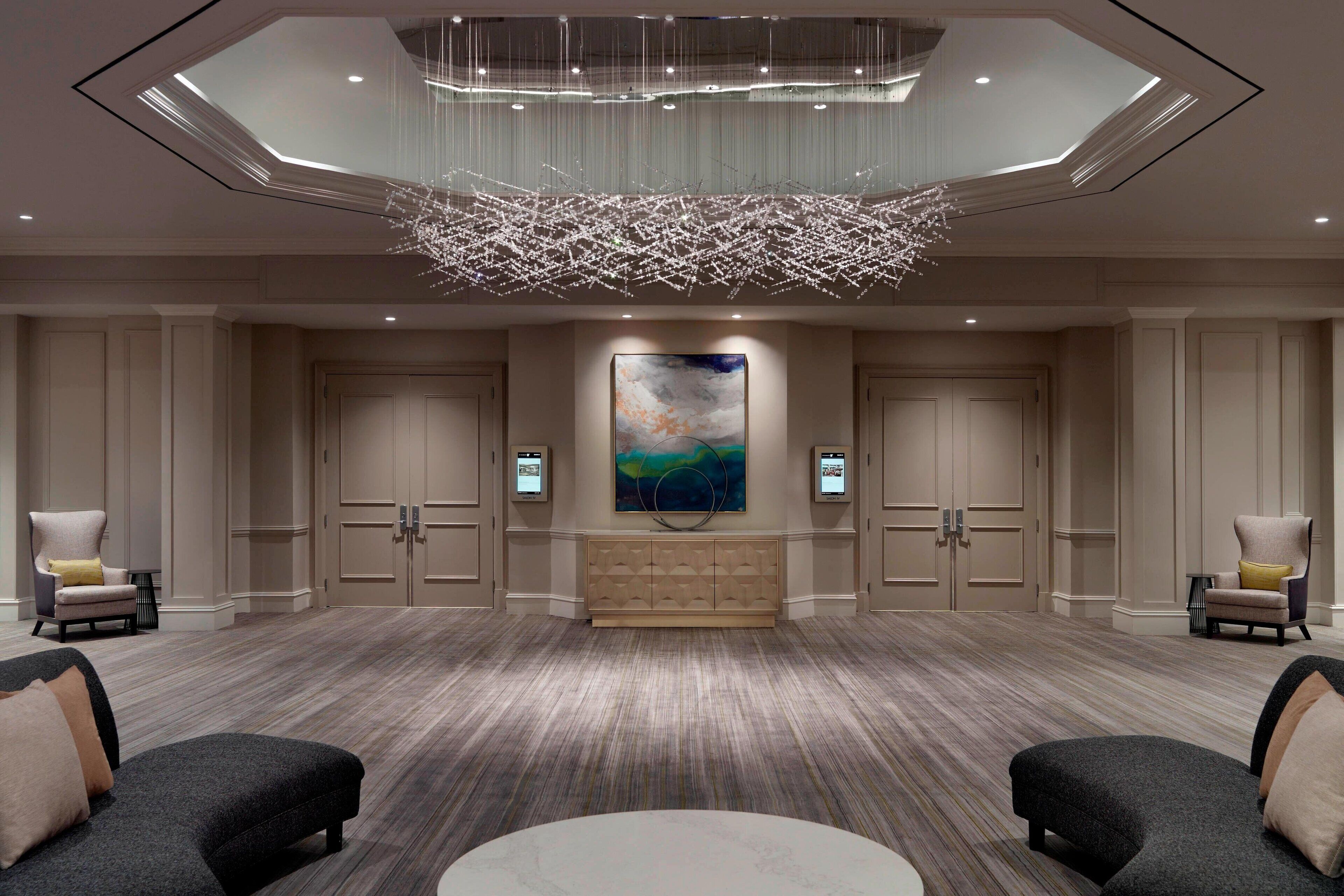 A spacious lobby with a modern chandelier, a large abstract painting, and a seating area with sofas and armchairs.