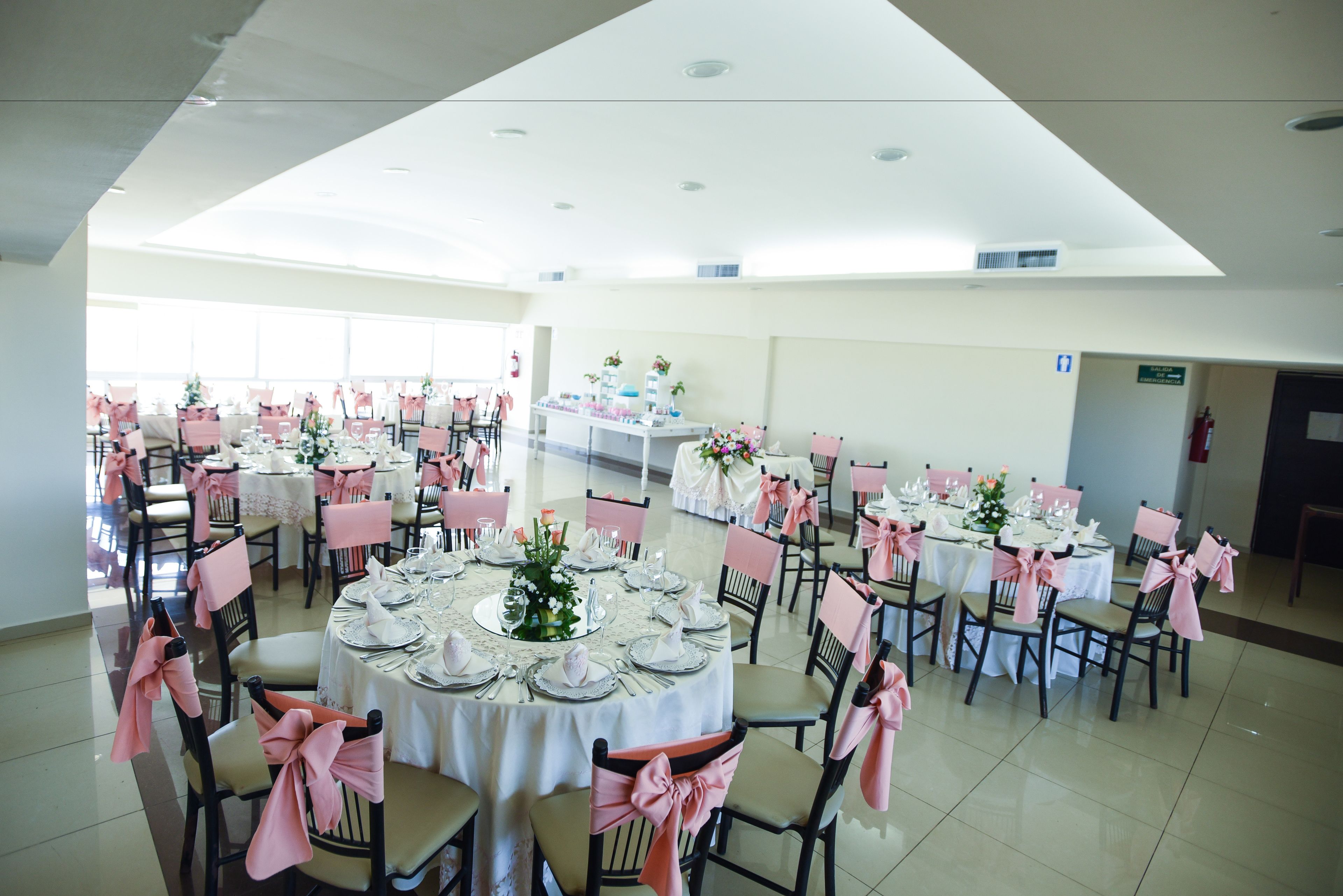 A spacious banquet hall with round tables set for dining, each with pink chair covers and white tablecloths.