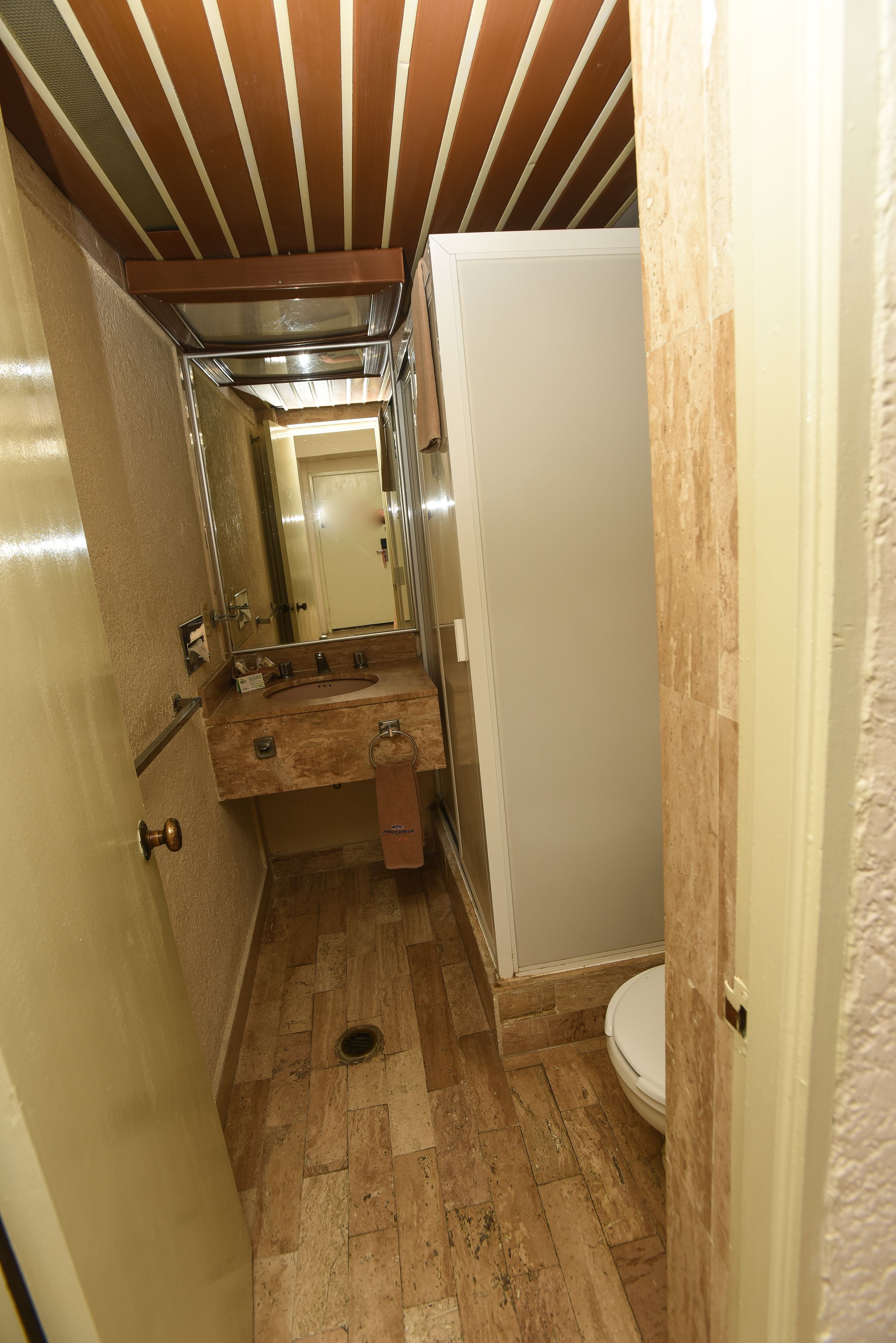 A narrow bathroom with a wooden ceiling, a sink with a mirror, and a toilet.