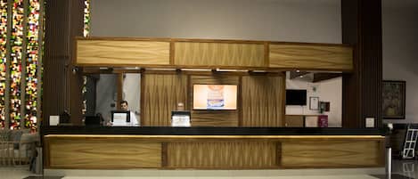 Un mostrador de recepción con detalles de madera, una pantalla digital y un reloj en la pared.