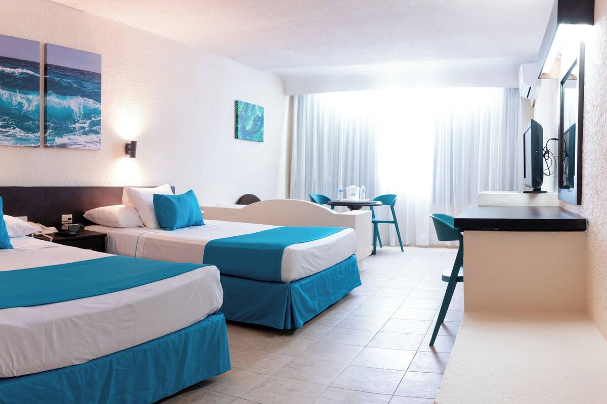 Ein Hotelzimmer mit zwei Betten, einem Schreibtisch, einem Stuhl und Kunstwerken an den Wänden.