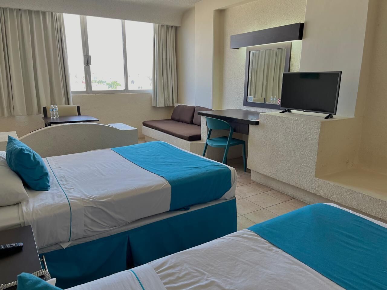 A hotel room with two beds, a desk, a chair, a TV, and a window with curtains.