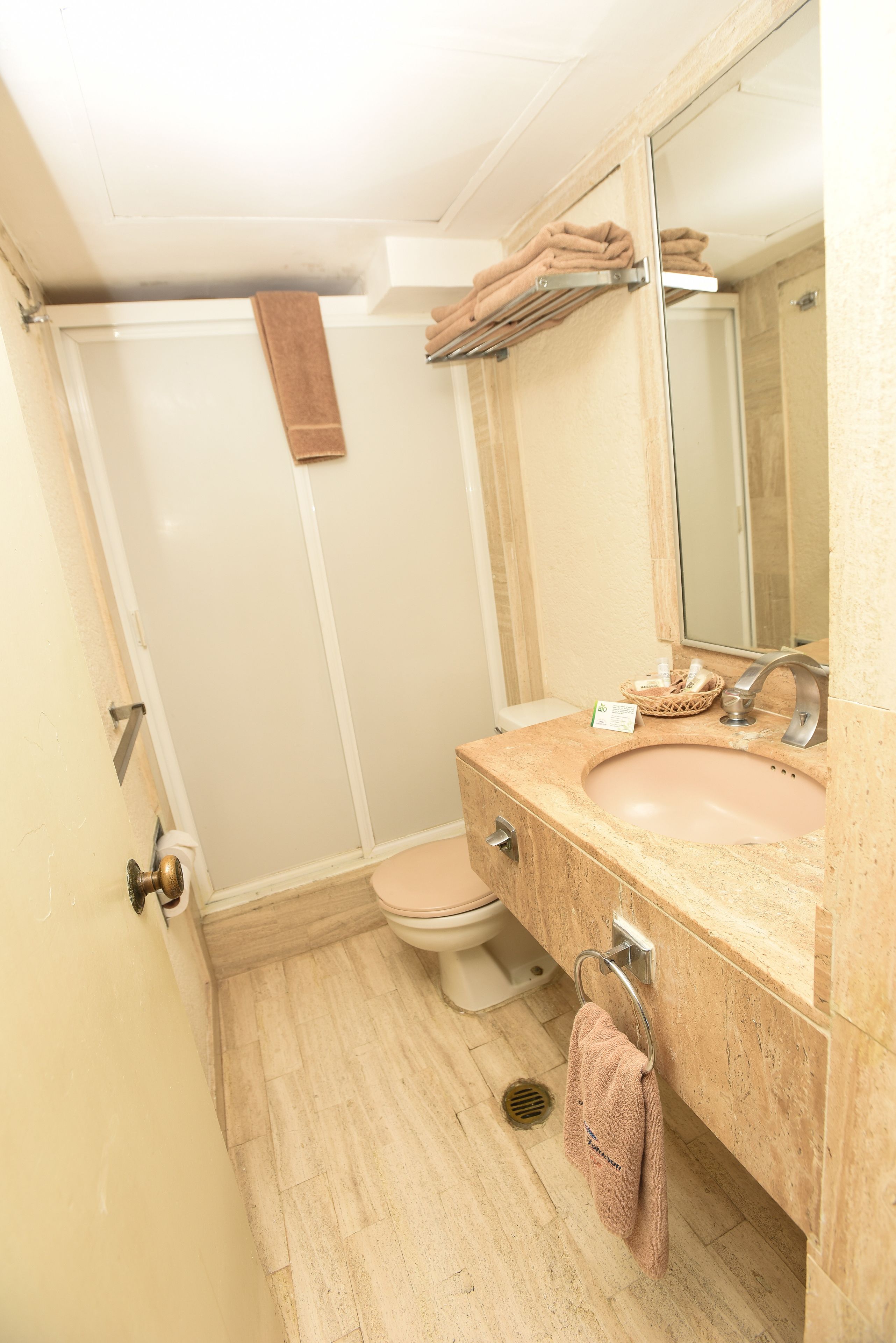 A bathroom with a toilet, sink, mirror, towel rack, and shower area.