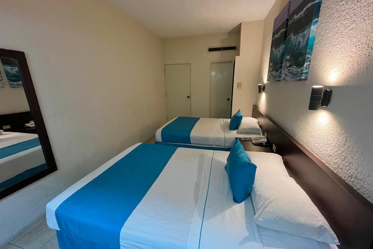 Ein Hotelzimmer mit zwei Betten, jeweils mit blau-weißer Bettwäsche, einem Nachttisch, einem Spiegel und einer wandmontierten Leuchte.
