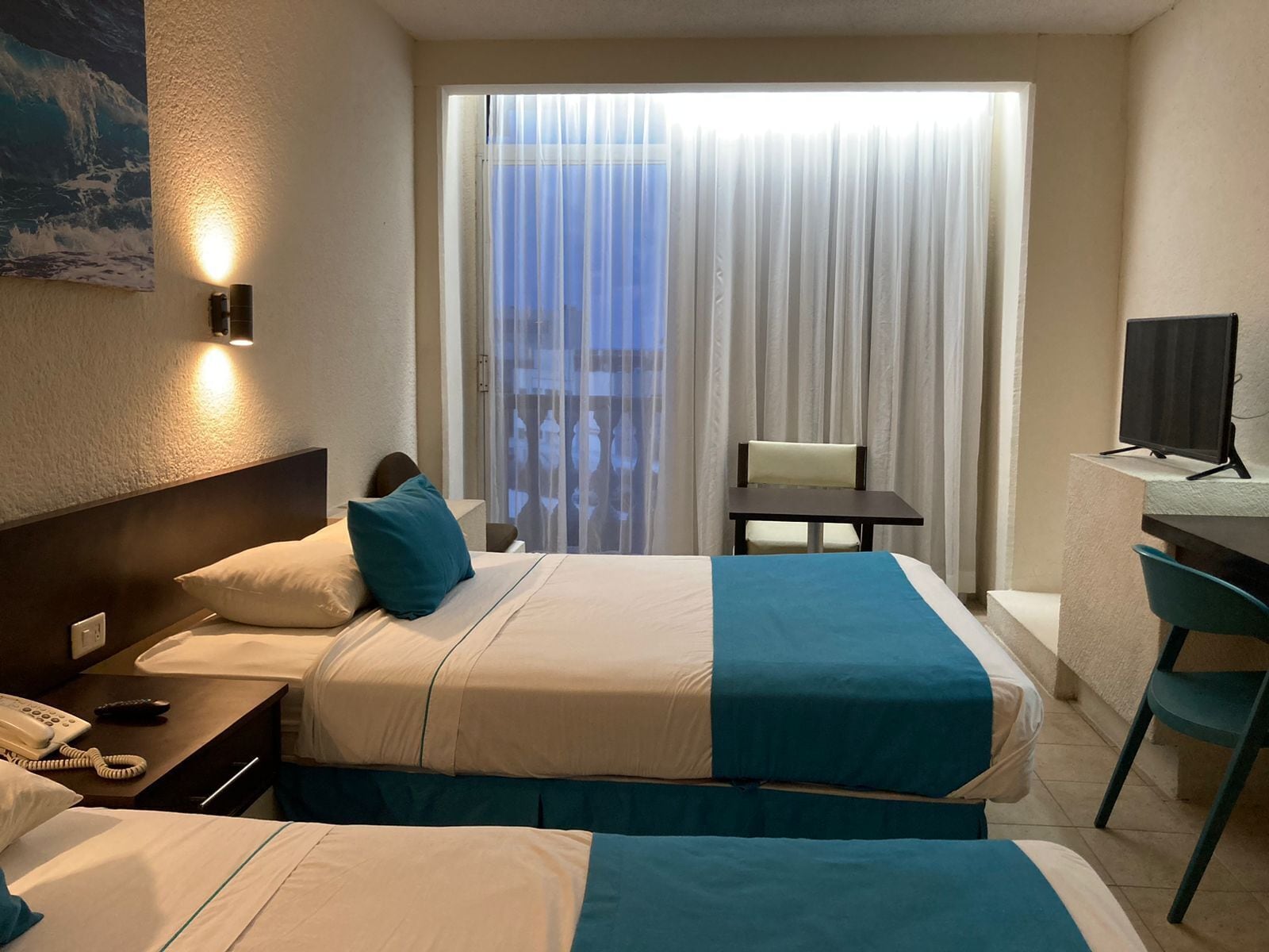 A hotel room with two beds, a desk, a chair, a TV, and a window with curtains.