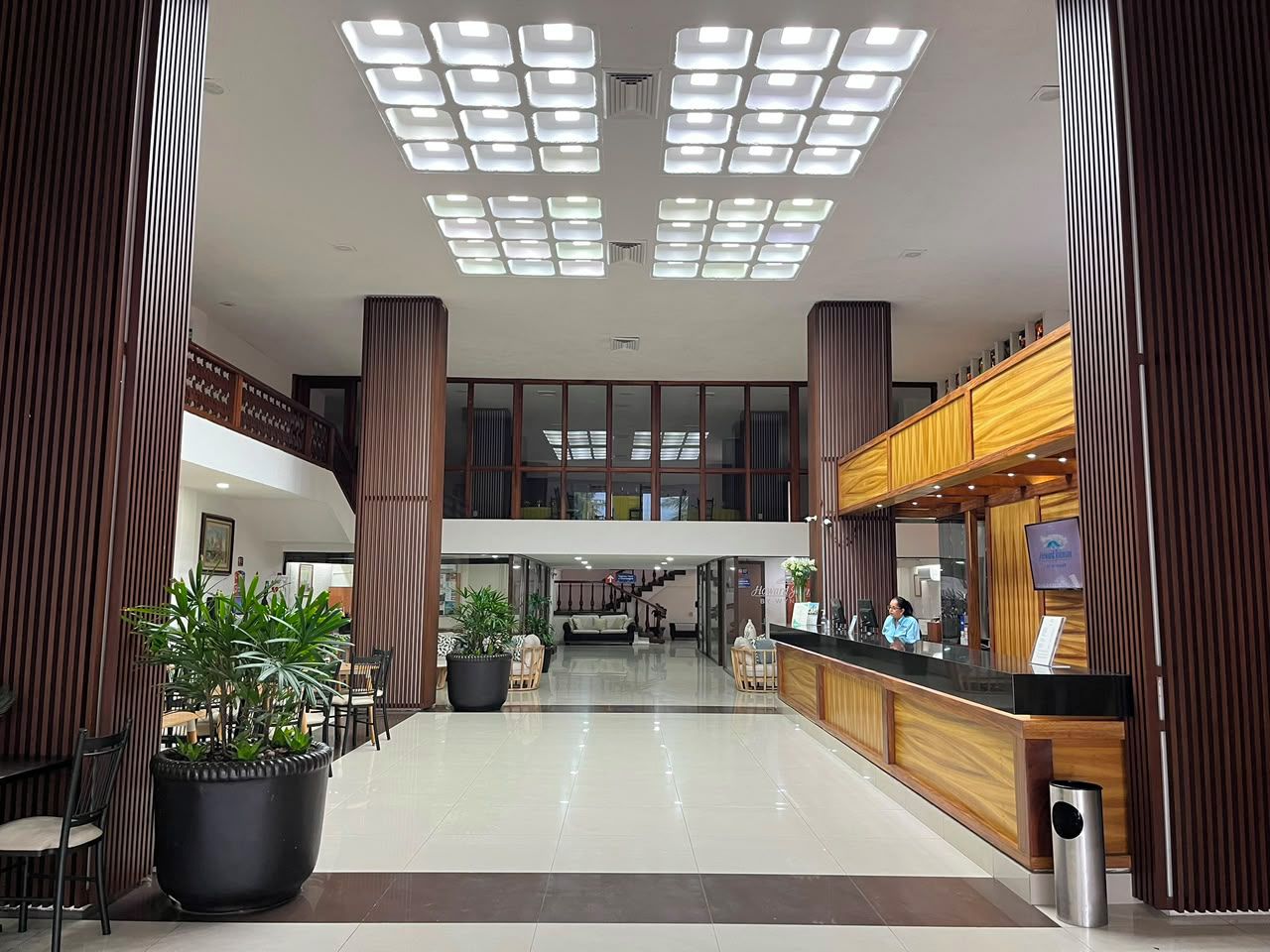 Een hotel lobby met een receptiebalie, een zithoek en een trap naar een hoger niveau.