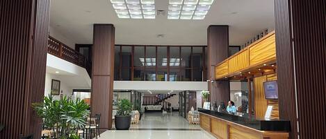 A hotel lobby with a reception desk, seating area, and a staircase leading to an upper level.