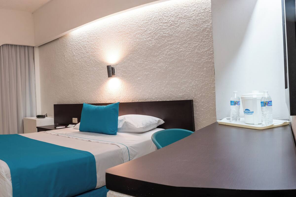 Ein Hotelzimmer mit Bett, Schreibtisch, Fernseher und einem durchgegangenen Tür sichtbaren Badezimmer.