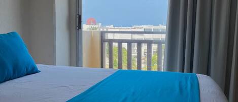 Una habitación de hotel con cama, vistas a la ciudad y un balcón con cortinas.