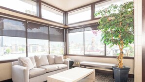 Habitació d'angle amb sofà, taula de café, una planta en test i grans finestres que donen vista a l'exterior.
