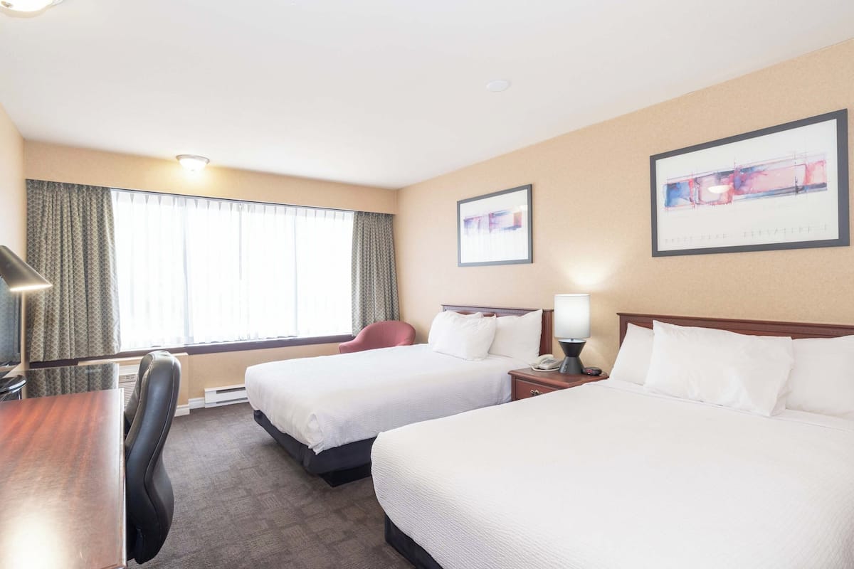 Habitación de hotel con dos camas, un escritorio, una silla, una ventana con cortinas y un cuadro en la pared.