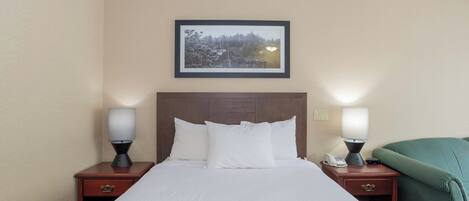 Una habitación de hotel con una cama grande, dos mesitas de noche con lámparas, un cuadro en la pared y una manta verde sobre la cama.