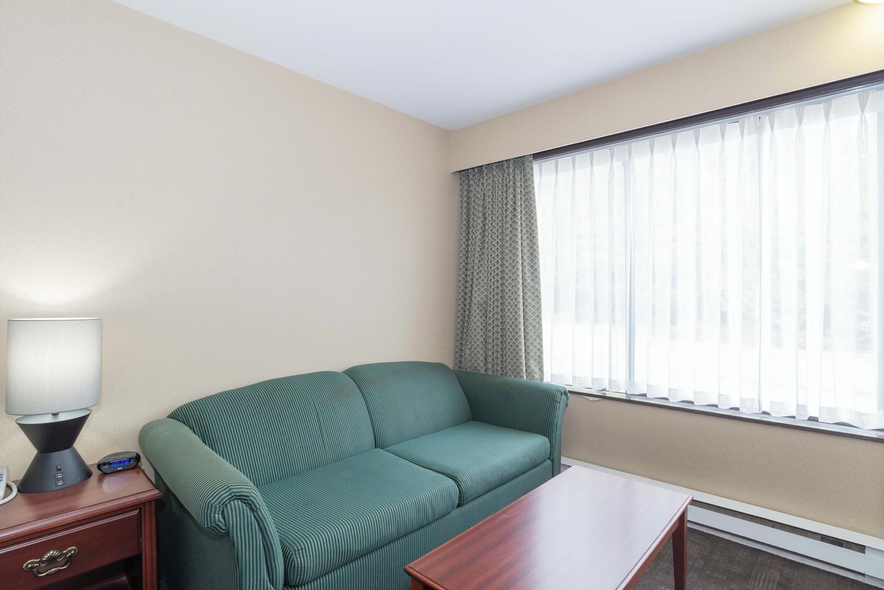 A room with a green sofa, a wooden nightstand with a lamp, and a table.